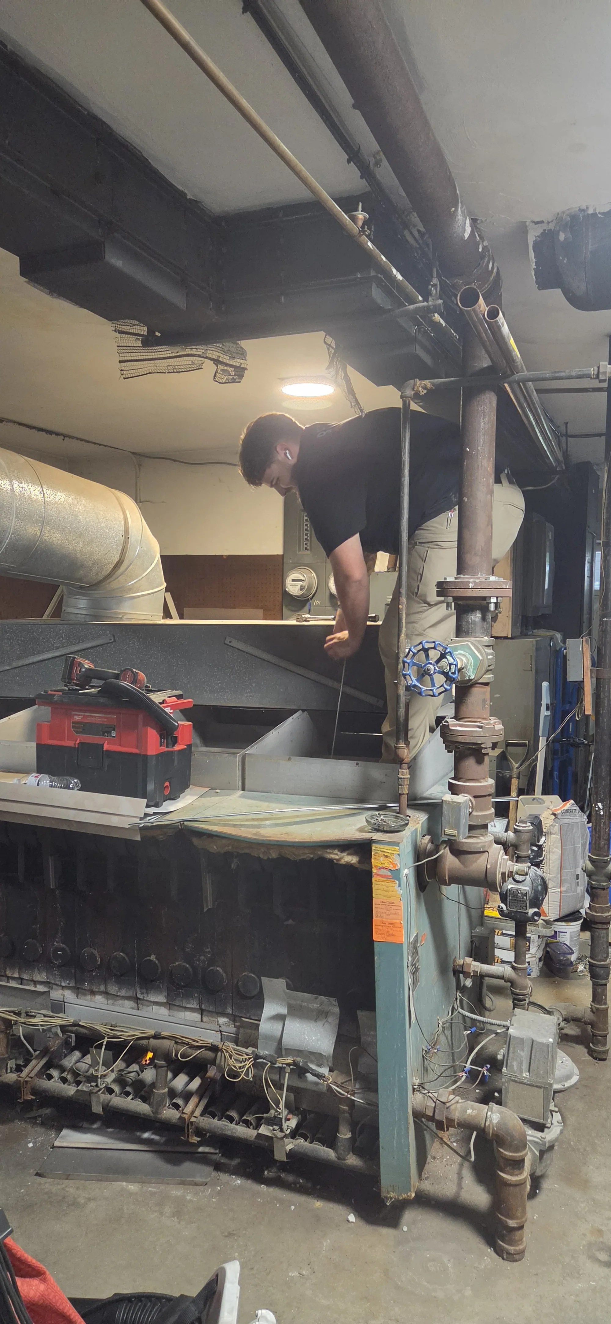 A technician working over a boiler in a boiler room during a heat exchanger cleaning in Cincinnati, OH, with a shop vacuum set on top of the unit.