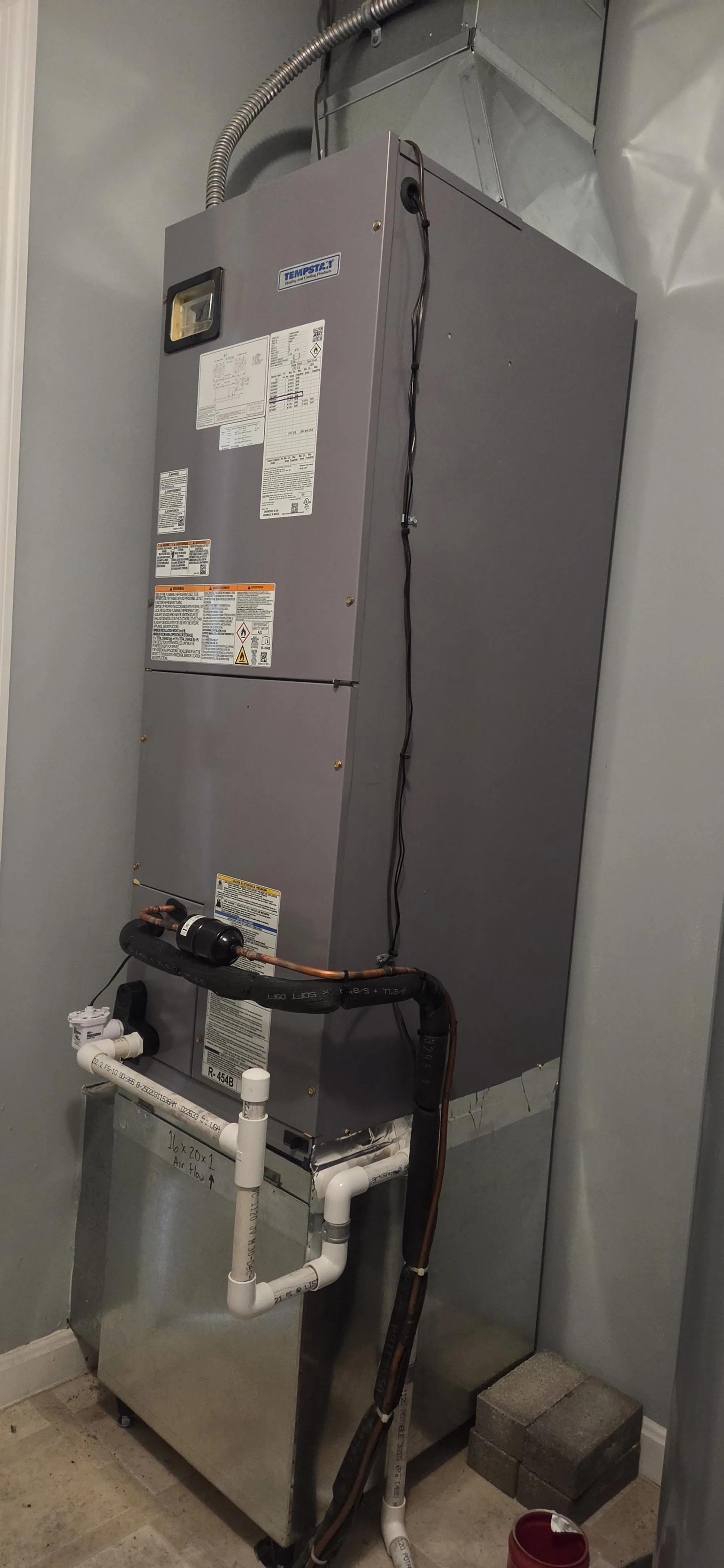 Electric furnace in a utility closet with insulated refrigerant lines and a white PVC condensate drain, HVAC job in Cincinnati, OH.